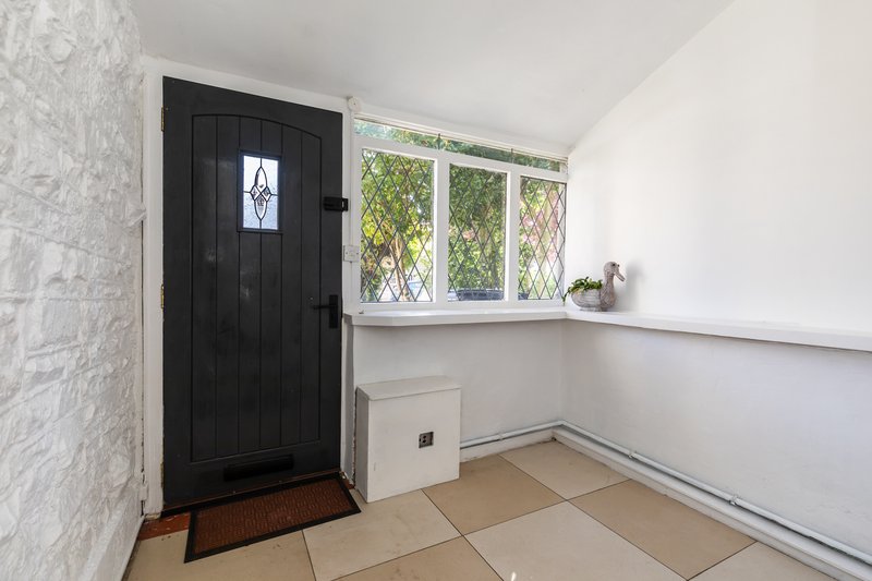 Entryway with black door, tiled floor, window with garden view and white wall panelling
