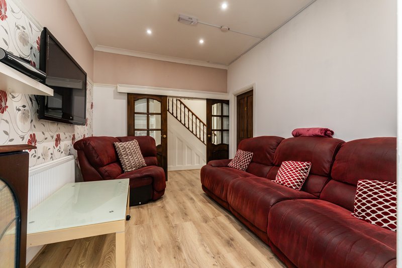 Open-plan living room with red sofas, white coffee table, wall-mounted TV and staircase