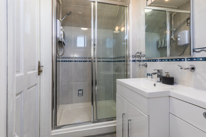 Modern bathroom with double vanity, white cabinetry, glass shower enclosure and blue tile accents