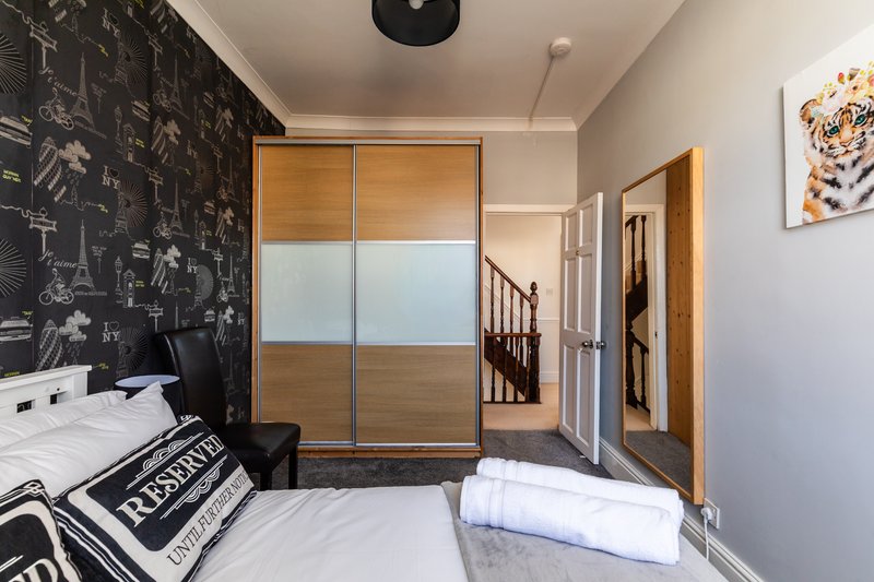 Modern bedroom with double bed, sliding wardrobe, black feature wall and staircase access