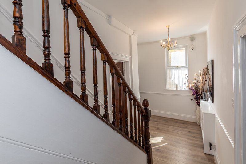 Bright hallway with wooden staircase, window, chandelier and hardwood flooring