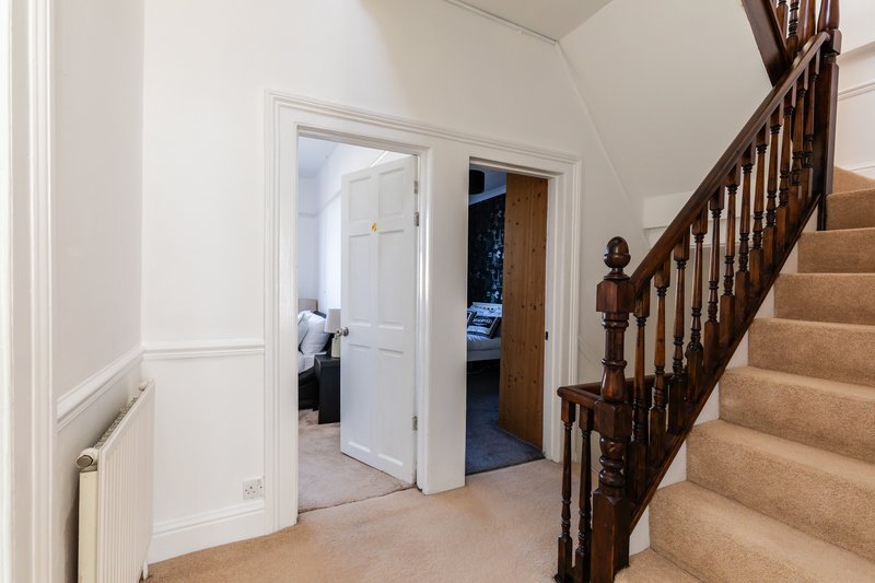 Hallway with wooden staircase, white doors, radiator, and cream carpet