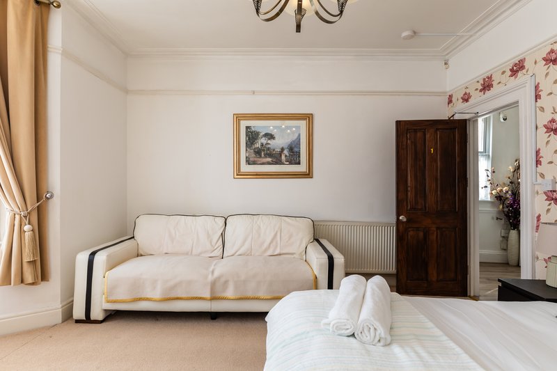 Spacious bedroom with cream sofa, white bed, framed artwork and wooden door