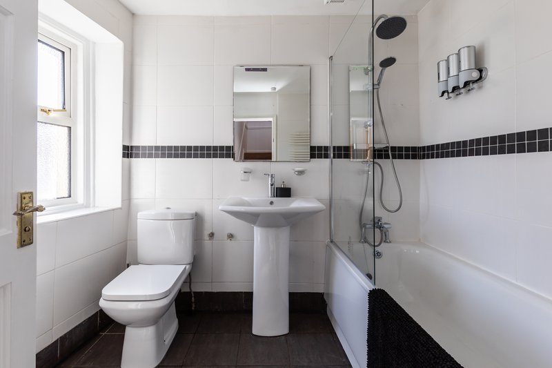 Modern bathroom with pedestal sink, toilet, shower enclosure and dark tile accents