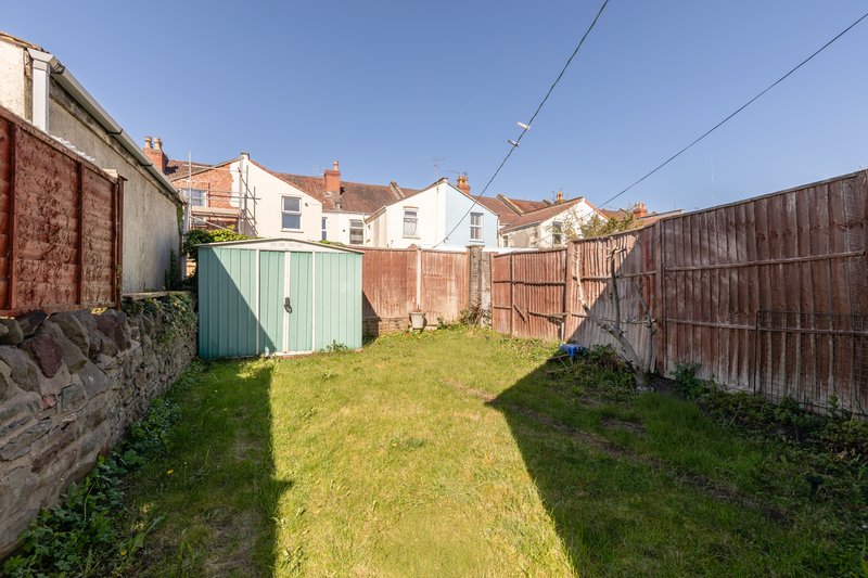 Enclosed garden with green lawn, wooden fencing, storage shed and neighbouring houses visible