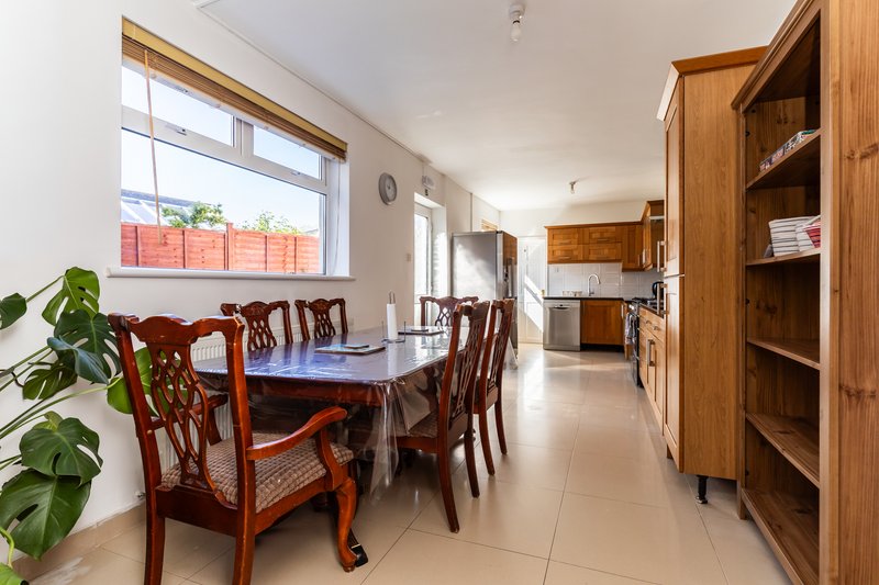 Bright dining room with wooden table, chairs, and kitchen visible in background