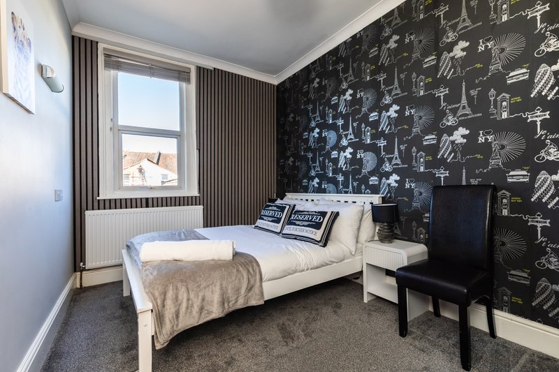 Bedroom with single bed, chalkboard accent wall, window with curtains, and desk chair