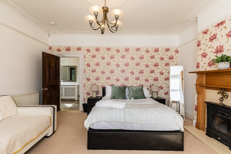 Spacious bedroom with double bed, floral wallpaper, fireplace and cream sofa