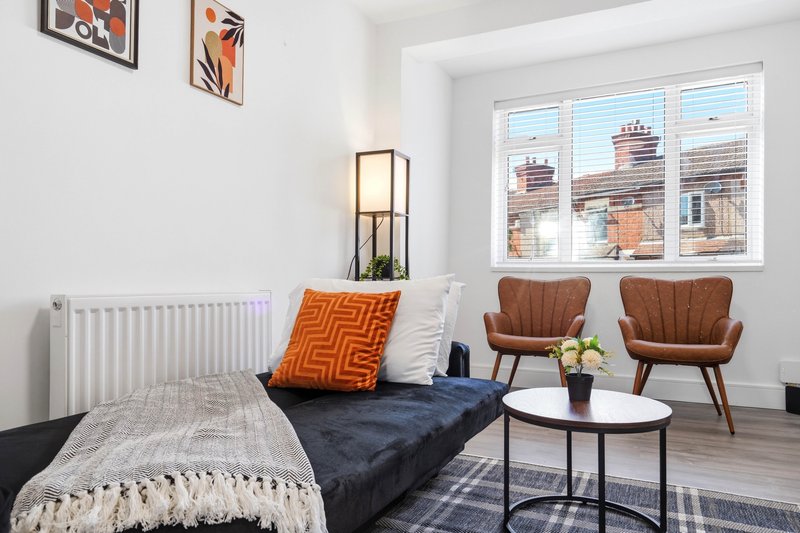 Modern bedroom with bed, orange cushion, brown armchairs, round table and large windows