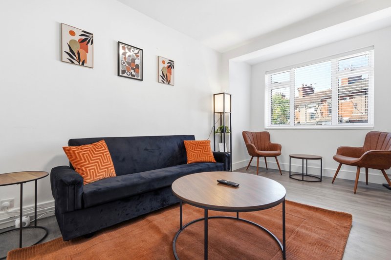 Bright living room with navy sofa, round wooden table, orange rug and modern wall art
