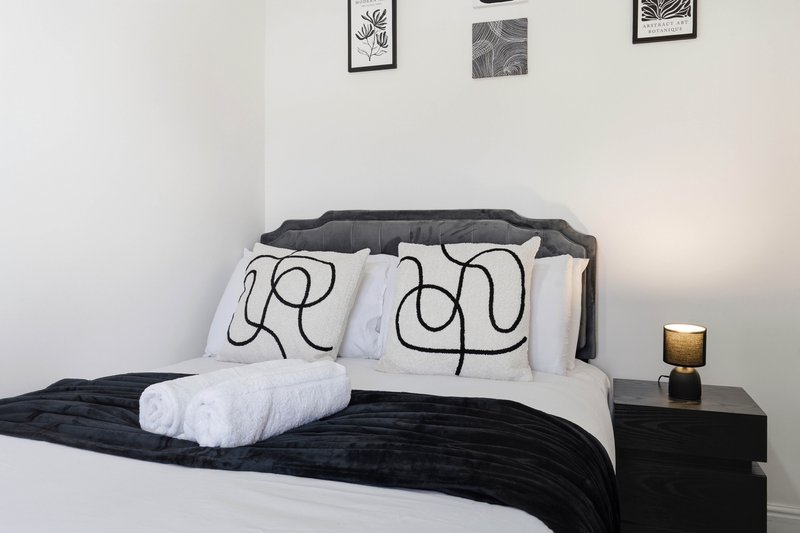 Modern bedroom with dark bed frame, white bedding, patterned pillows and wall art