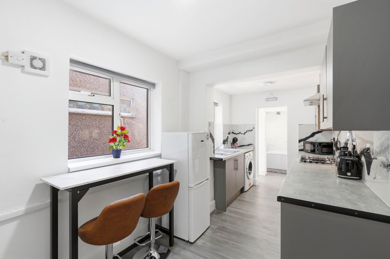 Modern kitchen with white countertops, black cabinetry, desk area with brown chairs and window