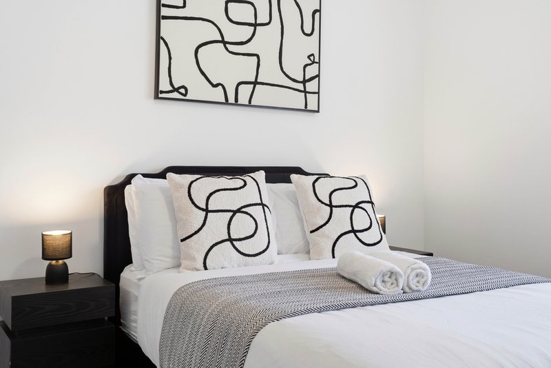 Modern bedroom with black bed frame, patterned pillows, rolled towels, and minimalist line-art wall decor