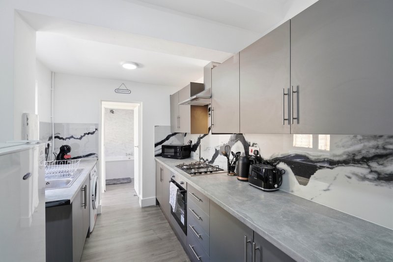 Modern kitchen with marble countertops, grey cabinetry, and view through to bedroom