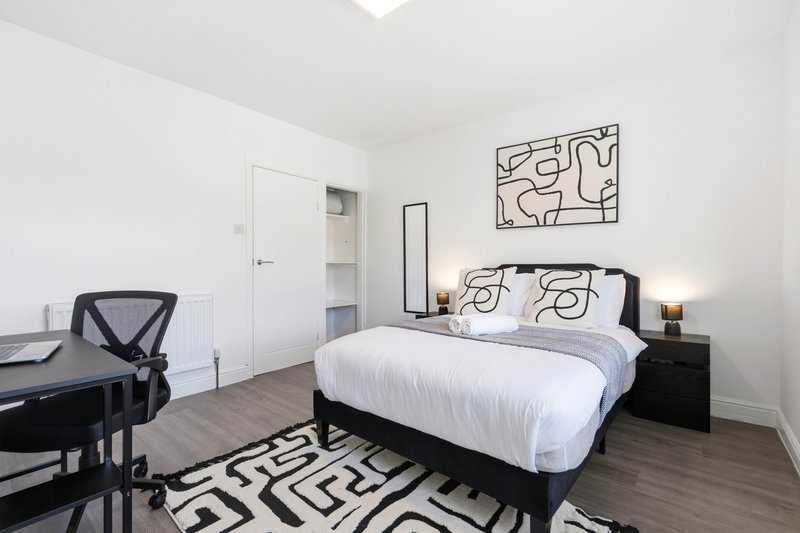 Modern bedroom with queen bed, black desk, geometric wall art and patterned rug