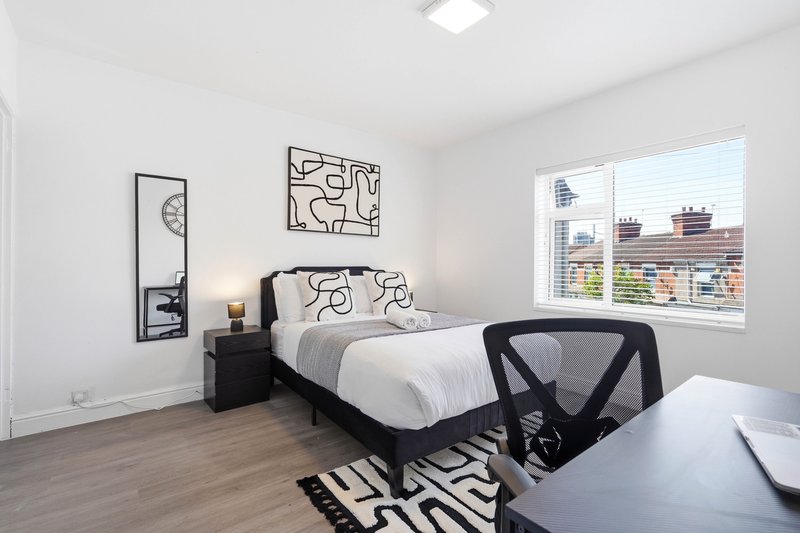 Modern bedroom with black bed frame, white bedding, desk chair, and city skyline view