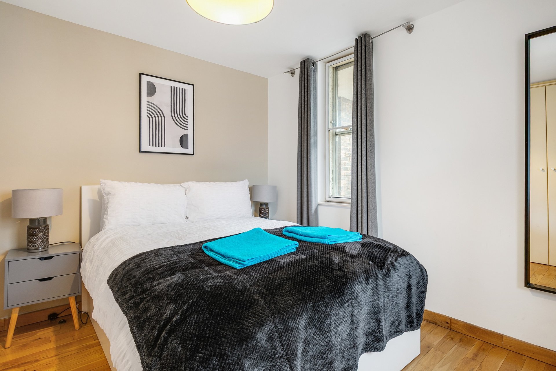 Bright bedroom with double bed, black throw blanket, white pillows, and bedside lamp