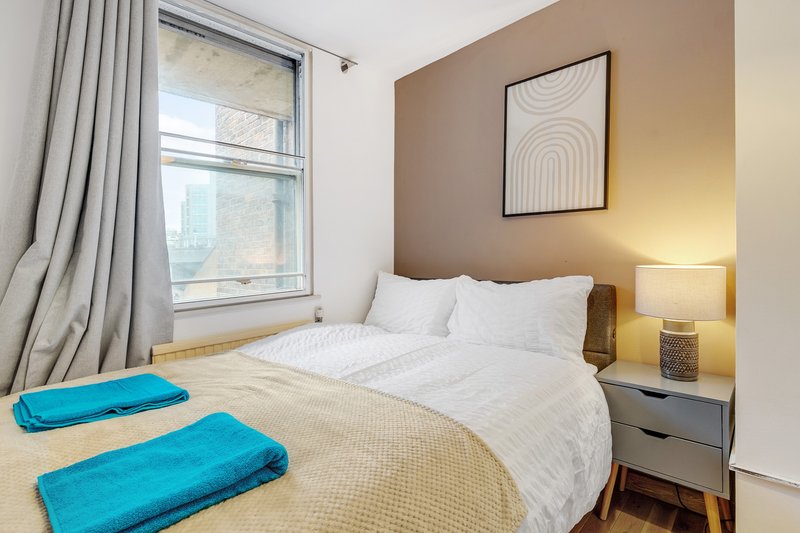 Bedroom with double bed, white bedding, two blue yoga mats, bedside lamp and framed wall art