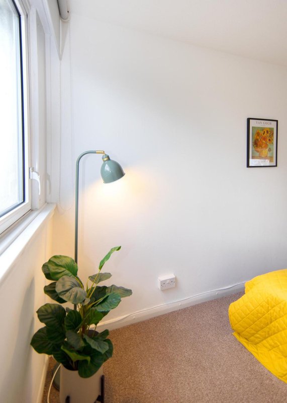 Bright bedroom corner with large window, floor lamp, potted plant and yellow cushion