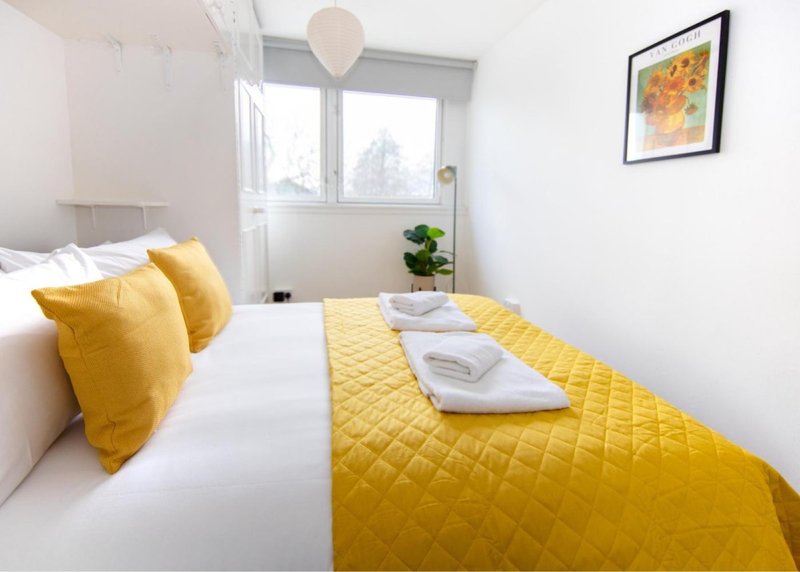 Bright bedroom with double bed, yellow bedding, cushions, and framed artwork on wall