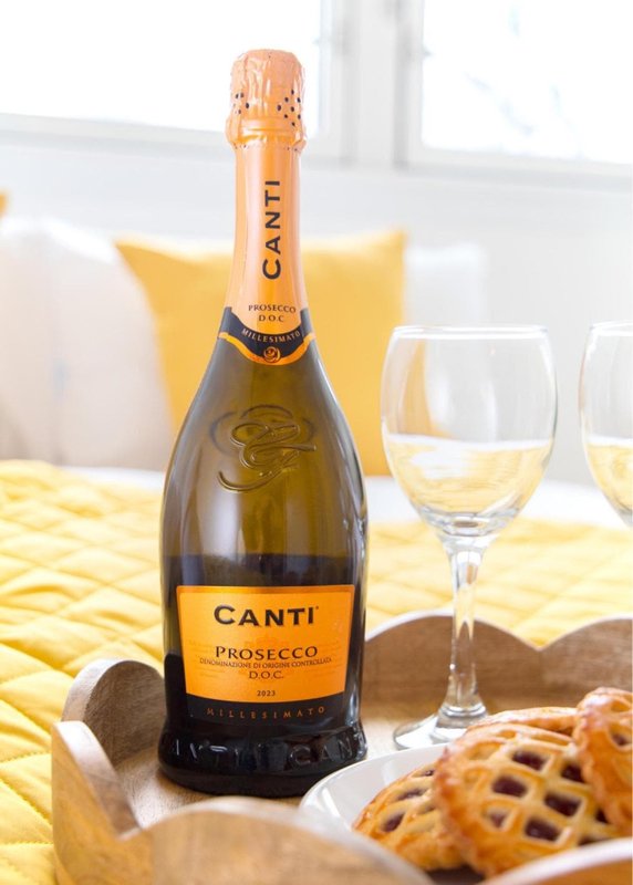 Bottle of Canti Prosecco with wine glasses and snacks on yellow table cloth