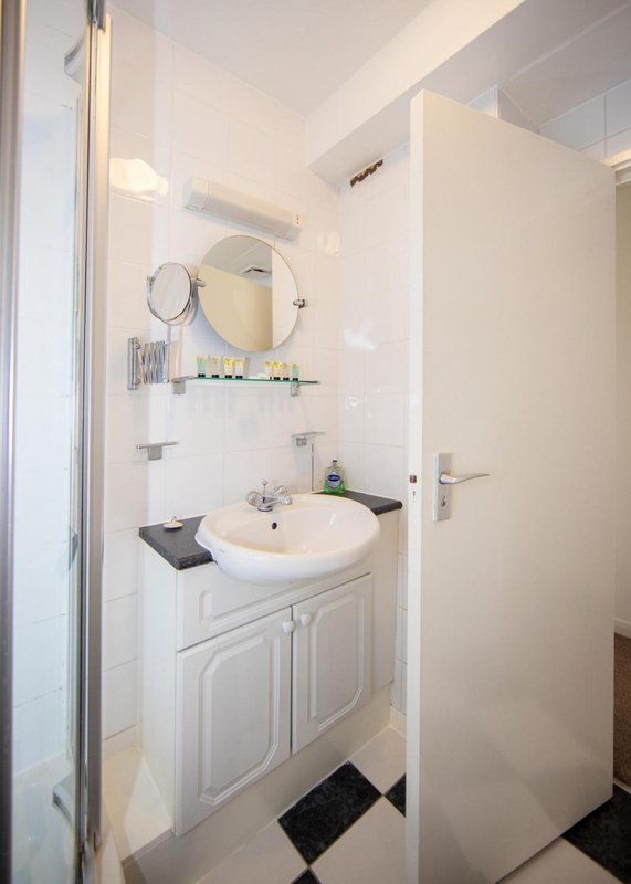 Clean white bathroom with round mirror, sink, vanity cabinet and black floor mat