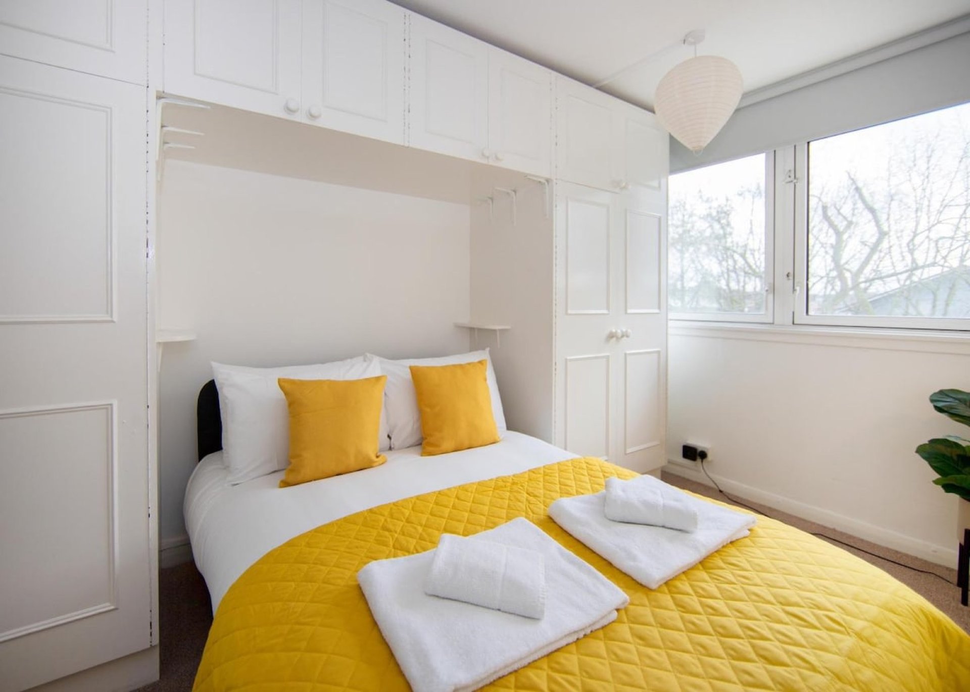 Bright modern bedroom with yellow bedding, white pillows, built-in wardrobe and window