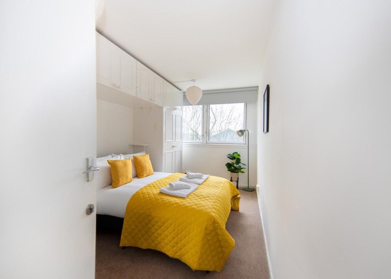 Bright modern bedroom with yellow bedding, single bed, window and potted plant