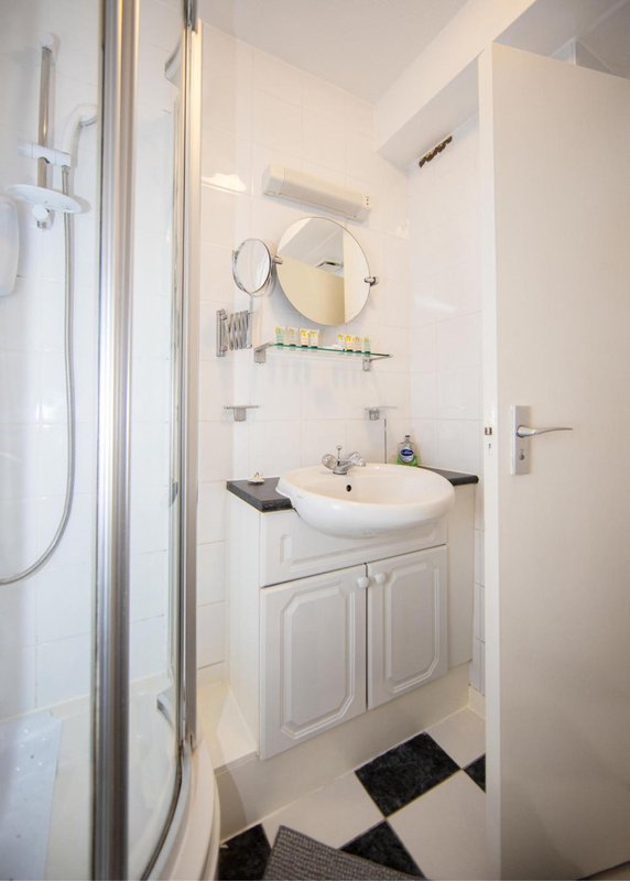 Bright bathroom with white vanity, round mirror, shower enclosure and geometric floor tiles