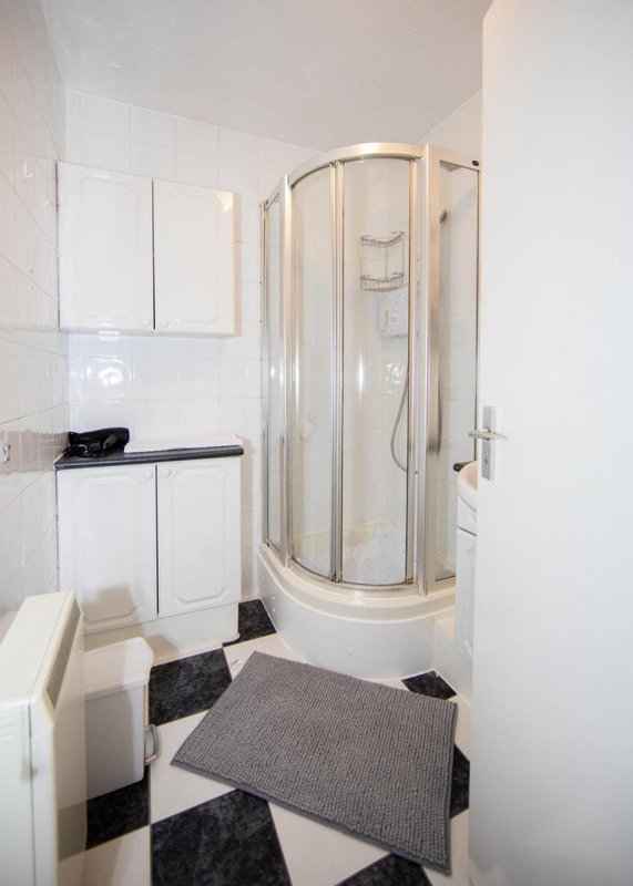 Modern bathroom with curved shower enclosure, vanity sink, white tiles and geometric floor mat