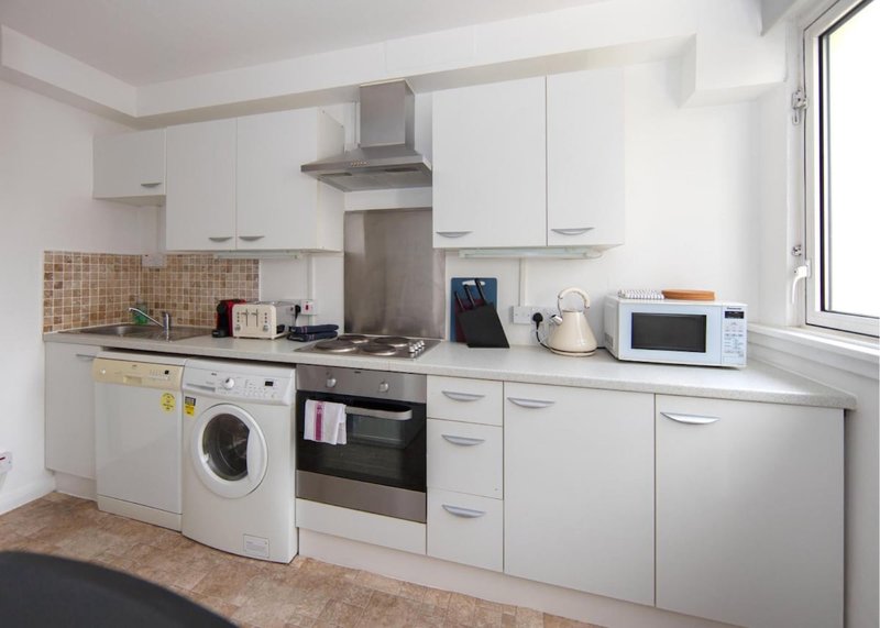 Modern white kitchen with integrated appliances, gas hob, washing machine and window