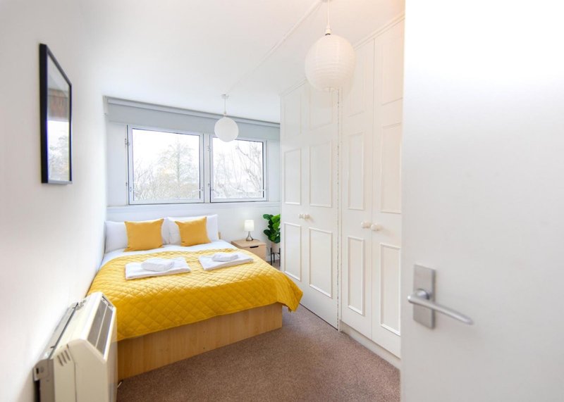 Bright bedroom with yellow bedding, double bed, window, white wardrobe and pendant lights