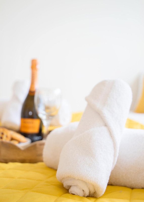 Rolled white towels on yellow surface with champagne bottle and glasses blurred background