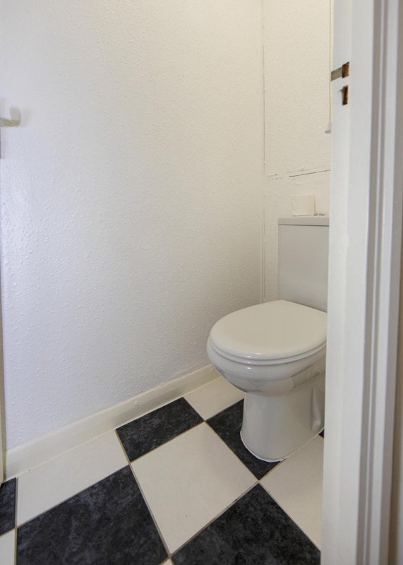 Small bathroom with white toilet, black and white checkered floor tiles, white walls