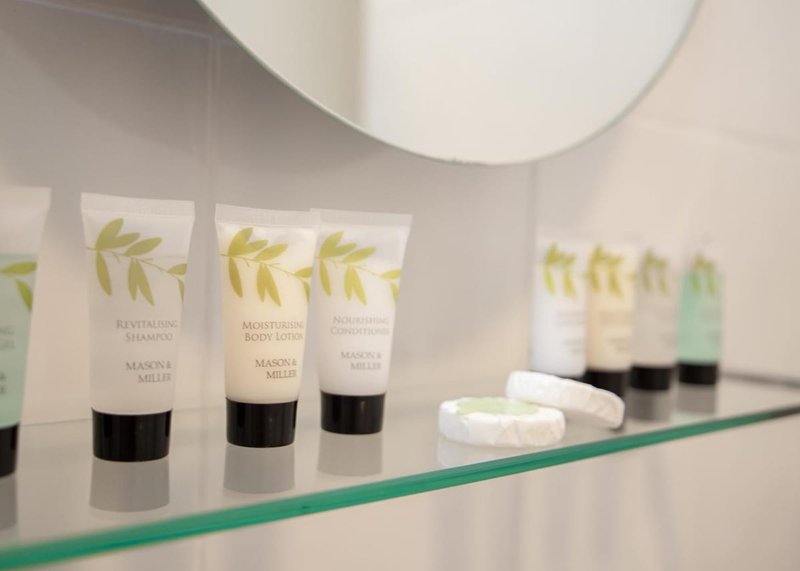 Bathroom shelf with branded toiletry bottles, white towels and circular mirror