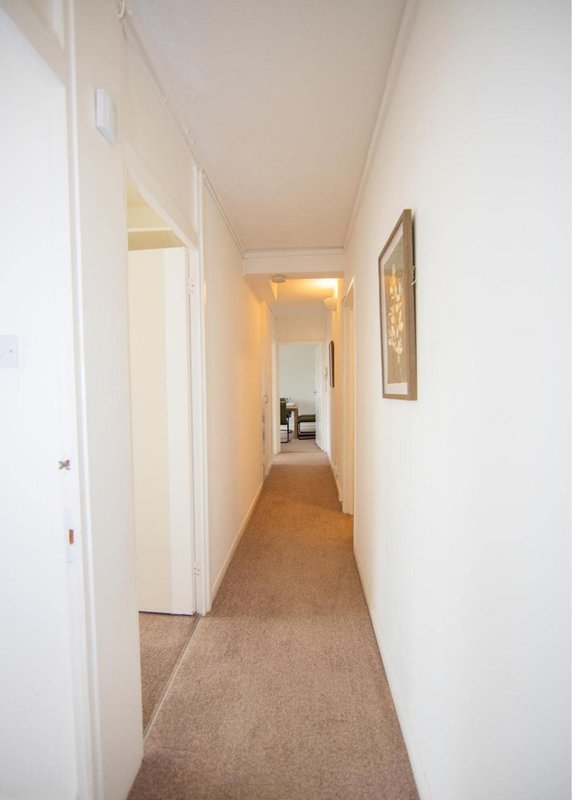 Long narrow hallway with beige carpet, white walls, doors, and framed artwork