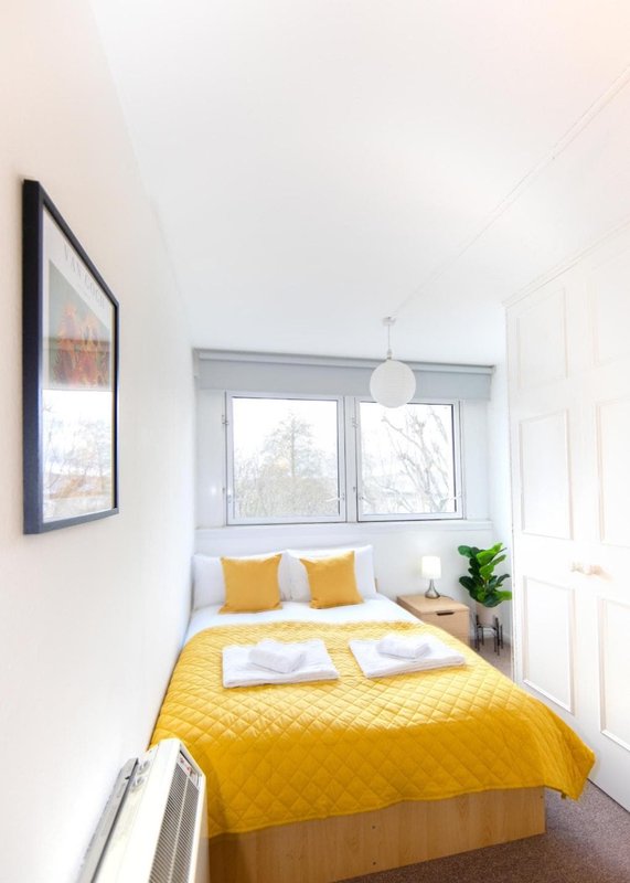 Bright bedroom with double bed, yellow bedding, framed artwork, window with view, and potted plant