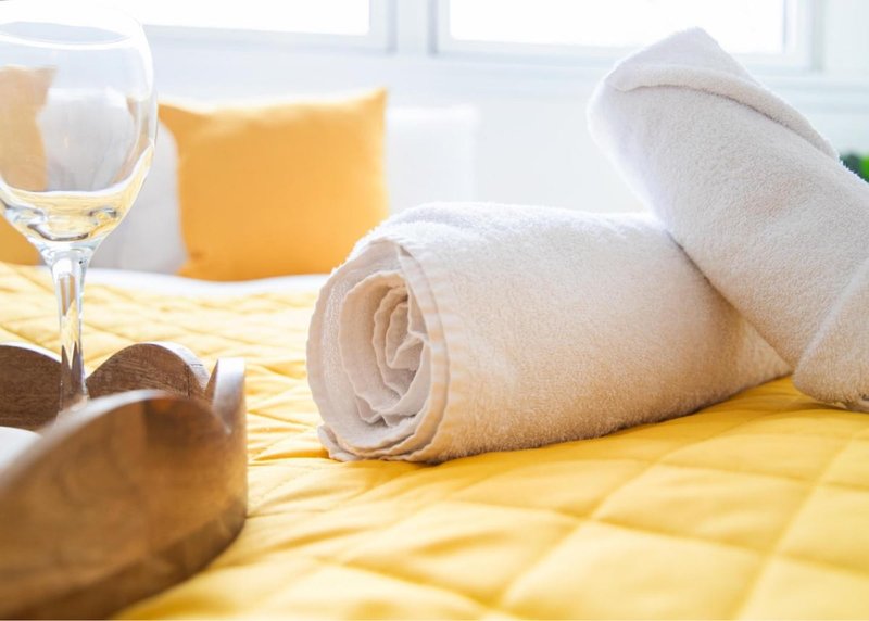 Bedroom with rolled white towels, yellow bedding, wine glass and decorative pillow