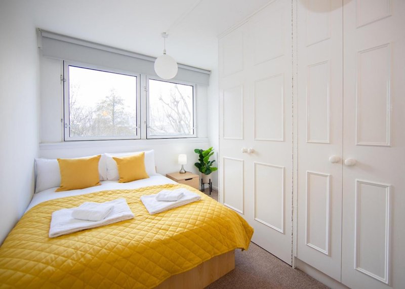 Bright bedroom with yellow quilted bedding, white pillows, large window and built-in wardrobes
