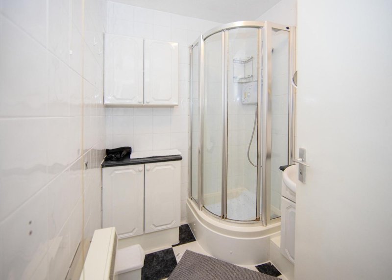 Clean white bathroom with corner shower enclosure, toilet, sink and storage cabinets