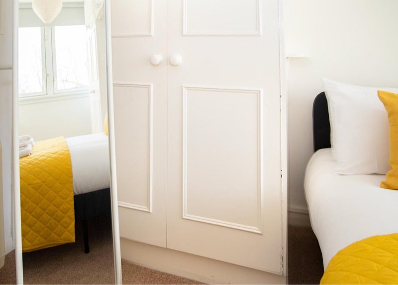 Bright bedroom with two single beds, yellow bedding, white pillows, and mirrored wardrobe