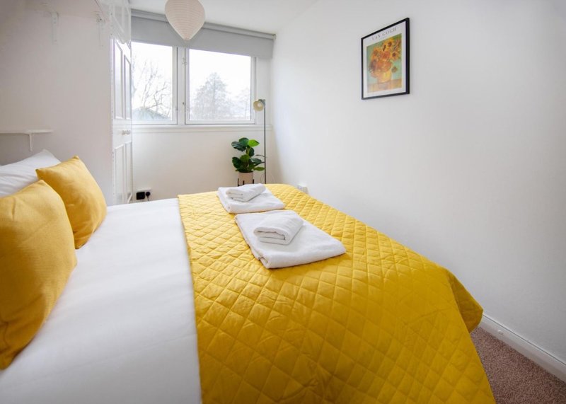 Bedroom with double bed, yellow quilted bedding, white pillows, and window with natural light