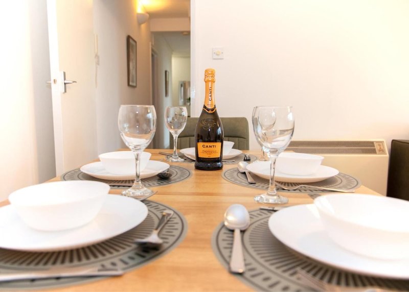 Dining table set with white plates, wine glasses, and champagne bottle in apartment