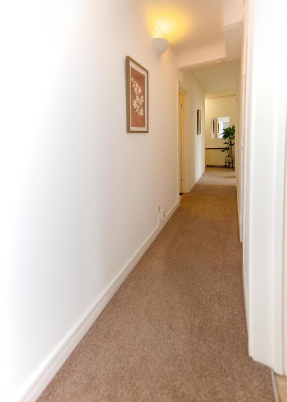 Long narrow hallway with beige carpet, white walls, framed artwork and wall lamp