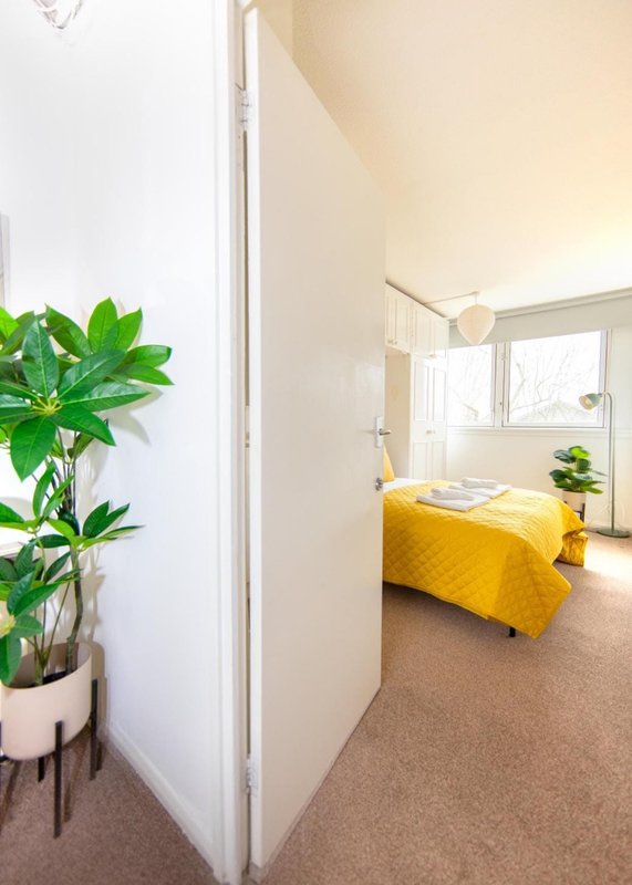 Bright bedroom with yellow bedding, potted plant in foreground, and natural window light
