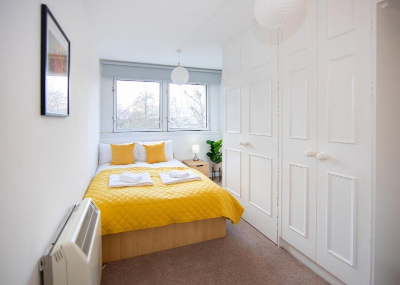 Bright bedroom with yellow bedding, wooden bed frame, window, white wardrobe and pendant light