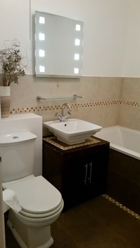 Modern bathroom with illuminated mirror, vessel sink, toilet and bathtub
