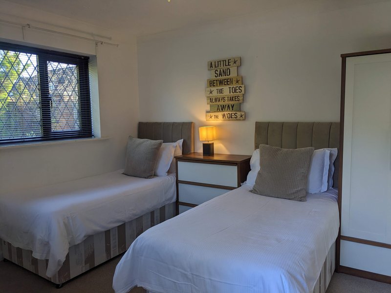 Twin bedroom with two single beds, wooden headboards, bedside table with lamp and coastal decor sign