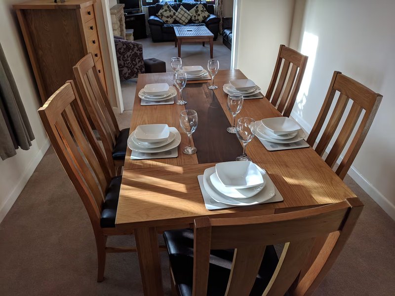 Dining room with wooden table set for four, upholstered chairs, and place settings