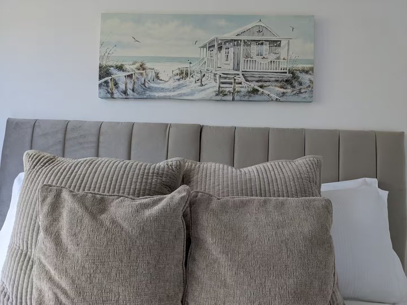 Bedroom with gray upholstered headboard, striped and patterned cushions, and beach house artwork